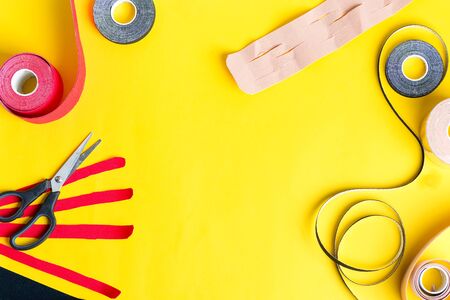 Set for kinesiology taping treatment from special physio tapes rolling of different colors and scissors for cutting on a yellow background, copy space. Top view. Kinesio treatment concept.の写真素材