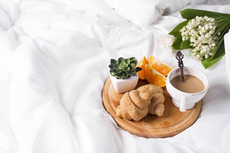 Coffee with milk and a bouquet of lilies of the valley in bed with a croissant and an orange. a place for the textの写真素材