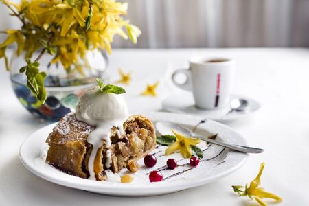 Apple strudel with vanilla ice cream and coffee, yellow flowers on a white backgroundの写真素材