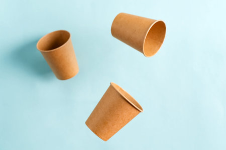 Paper mock-up eco-friendly disposable utensils floating cup above pastel blue background with soft...