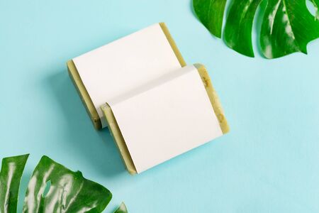 Natural cosmetic skin product handmade soap bar from organic plant ingredients with paper label on a green tropical leaf and pastel blue background. Mock-up for your design and creativity.の写真素材