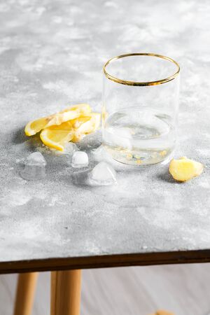 Freshly prepared homemade lemonade with lemon and ice cubes in glass with clear water on gray stone background. Cold summer nonalcoholic drink.の写真素材