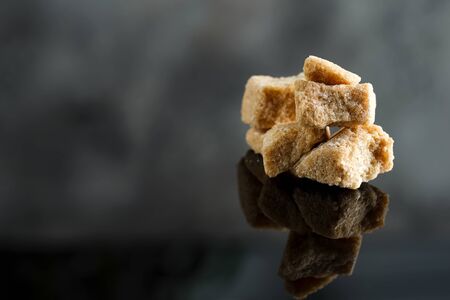 Heap from cubes of fresh natural brown cane sugar on a dark black background with reflection and copy space.の写真素材