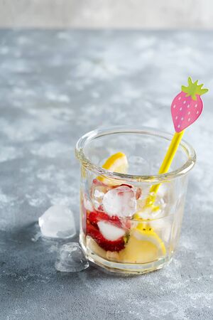 Homemade freshly prepared cold lemonade or cocktail from natural berries and lemon fruits in a glass with ice cubes on a light grey background, copy space. Cold summer nonalcoholic drink.の写真素材