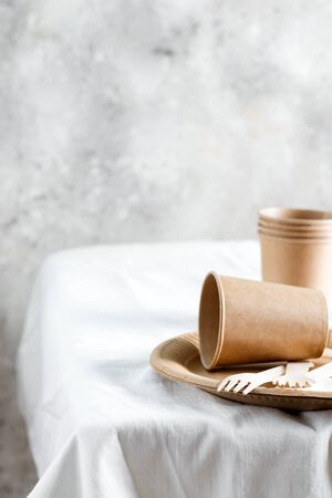 Empty disposable eco-friendly utensils - plates, cups and forks made from wooden and paper maretials on a white tablecloth against grey wall background, copy space.の写真素材