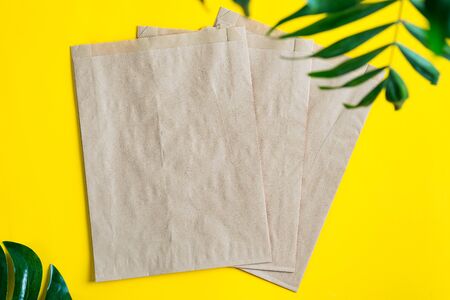 Eco friendly papercraft brown bags mockup for packaging different goods and things on a yellow background with green tropical leaves, copy space. Top view.の写真素材