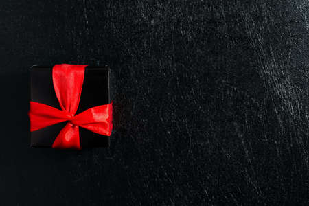 Gift box tied up with red ribbon on a black leather.の写真素材