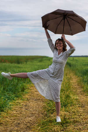 Beautiful woman with a brown umbrella wearing elegant dress pose in the field.の写真素材