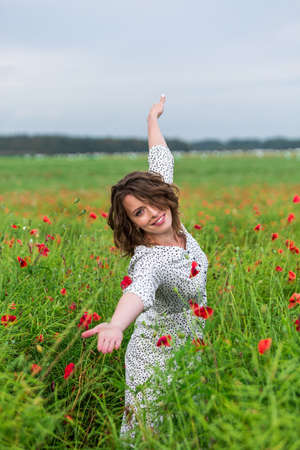Beautiful female pose in the field of red poppies in the warm summer evening.の写真素材