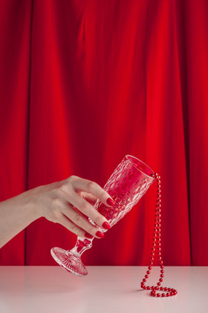 Hand with a red manicure hold a glass with beads for party on a table with a red cloth in the background.の写真素材