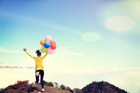 young cheering woman running with colorful balloons on mountain peakの写真素材