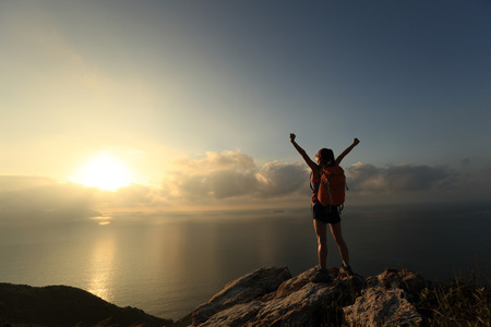 cheering young woman backpacker at sunrise seaside mountain peakの写真素材