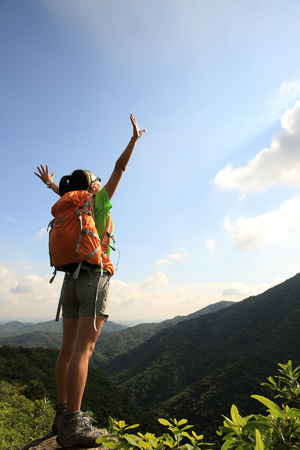 cheering young woman backpacker open arms on mountain peakの写真素材