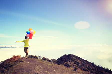 young cheering woman running with colorful balloons on mountain peakの写真素材