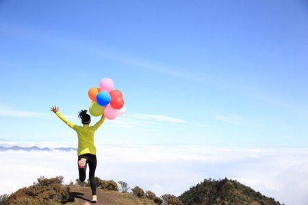 young cheering woman running with colorful balloons on mountain peakの写真素材