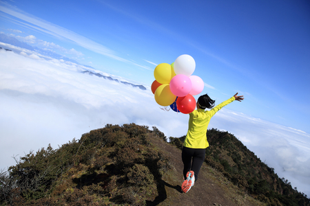 cheering young woman with colorful balloons on mountain peakの写真素材