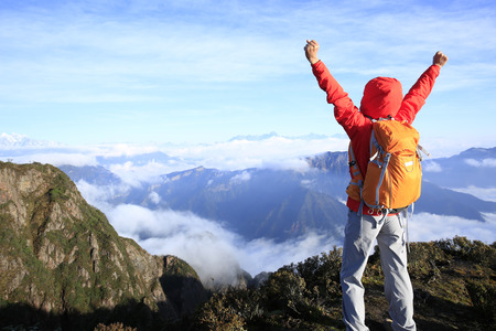 cheering young woman hiker open arms at mountain peakの写真素材