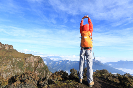 young woman backpacker stretching arms on beautiful mountain peakの写真素材