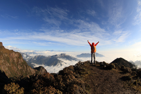 cheering young woman hiker open arms on mountain peakの写真素材