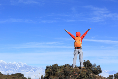 cheering young woman hiker open arms on mountain peakの写真素材
