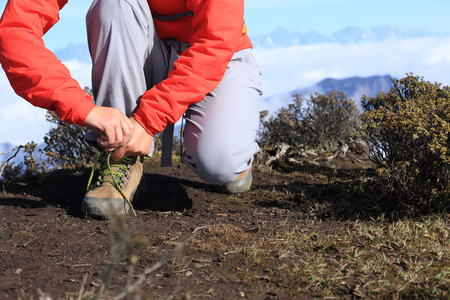 young woman hiker tying shoelace of hiking boots on mountain peakの写真素材