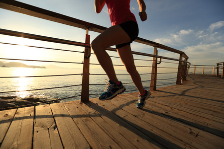 young fitness woman legs running on sunrise seaside trailの写真素材