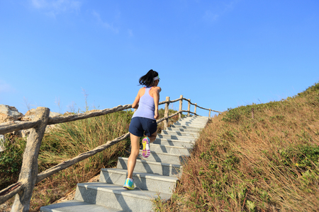 young fitness woman trail runner running up on mountain stairsの写真素材