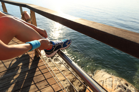 young fitness woman runner tying shoelace at seaside boardwalkの写真素材
