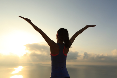 cheering young fitness woman at sunrise seasideの写真素材