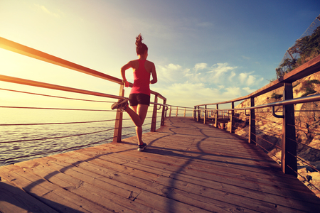 young fitness woman legs running on sunrise seaside boardwalkの写真素材