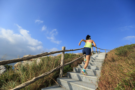 young fitness woman trail runner running up on mountain stairsの写真素材