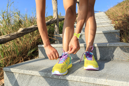 young woman runner tying shoelaces on stone trailの写真素材