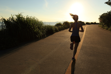 young fitness woman running on sunrise seaside trailの写真素材