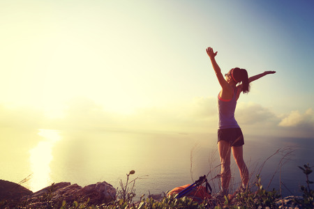 cheering young woman backpacker at sunrise seaside mountain peakの写真素材