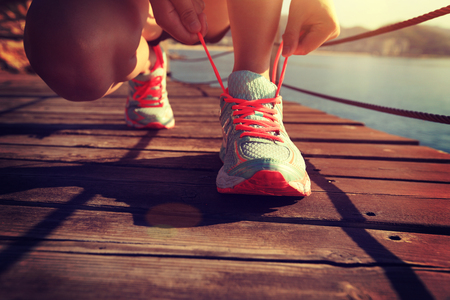 young fitness woman runner tying shoelace at seaside boardwalkの写真素材