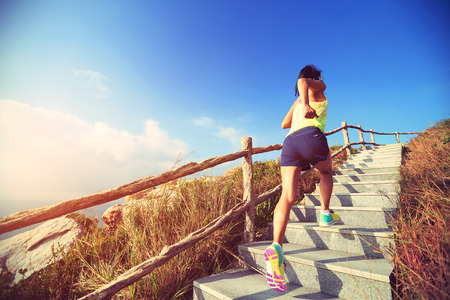 young fitness woman trail runner running up on mountain stairsの写真素材