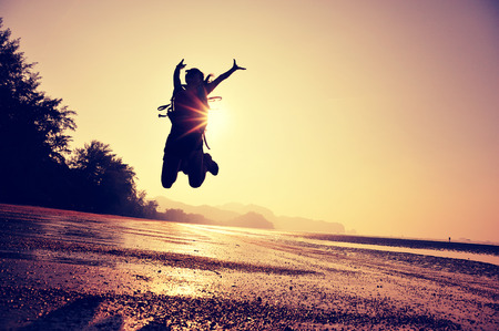 cheering young woman hiker jumping on sunrise beachの写真素材