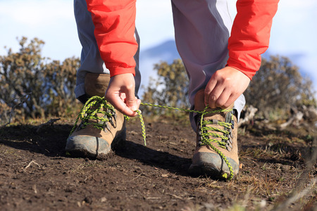 young woman hiker tying shoelace of hiking boots on mountain peakの写真素材