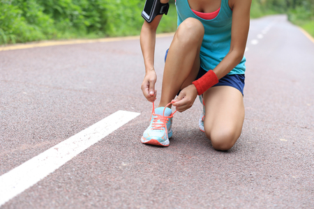 young woman runner tying shoelaces on trailの写真素材