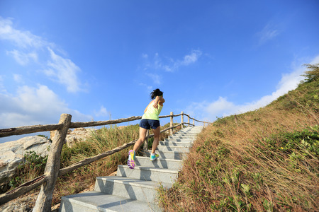 young fitness woman trail runner running up on mountain stairsの写真素材