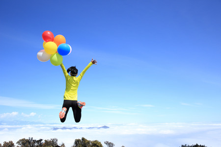 cheering young woman jumping on mountain peak with colorful balloonsの写真素材