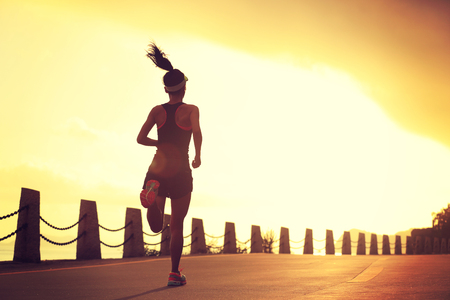young fitness woman running on sunrise seaside trailの写真素材