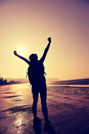 cheering young woman hiker on sunrise beachの写真素材