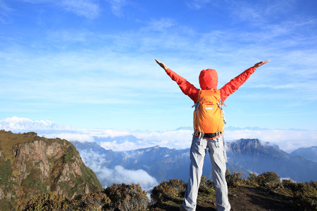 cheering young woman hiker open arms at mountain peakの写真素材