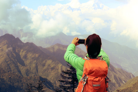 young asian woman backpacker taking photo with smartphone on mountain peakの写真素材
