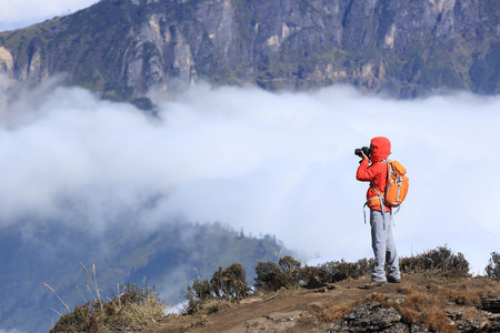 young woman photographer taking photo for beautiful landscape on mountain peakの写真素材