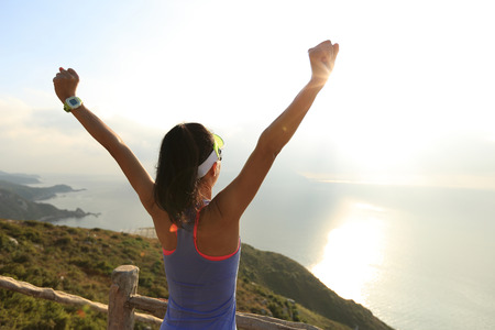 cheering young fitness woman open arms at sunrise seasideの写真素材