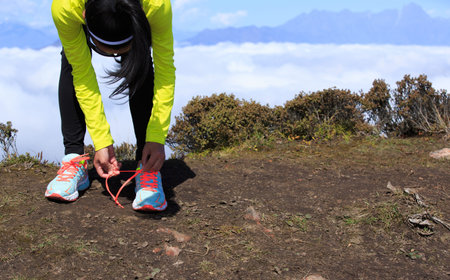 young woman trail runner tying shoelace on mountain peak