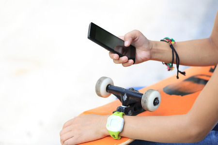 closeup of young woman skateboarder use smart phone in cityの写真素材