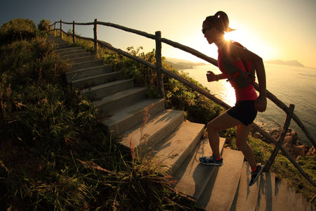 fitness woman trail runner running on seaside mountain stairs, training for cross country running.